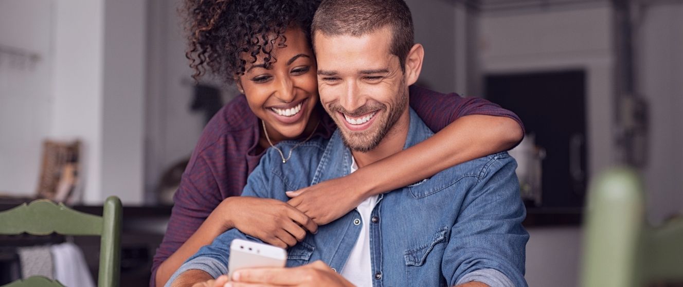 Happy adult couple smiling and looking at a smartphone together at home.